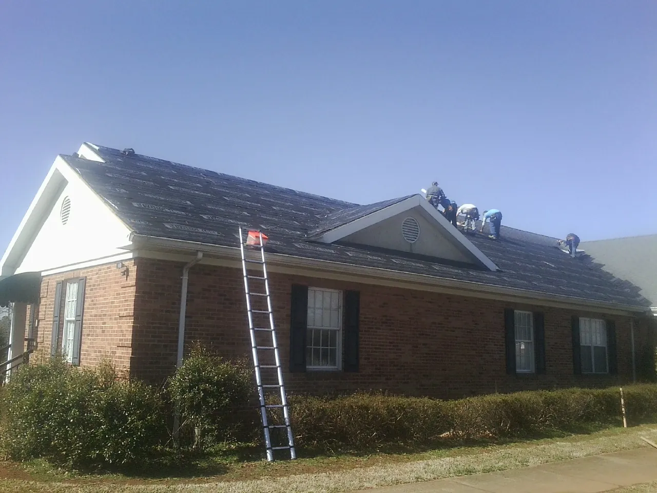 Crew tearing shingles off a brick ranch roof with a ladder set — Metal Roof Repair work by our crew in Seaford